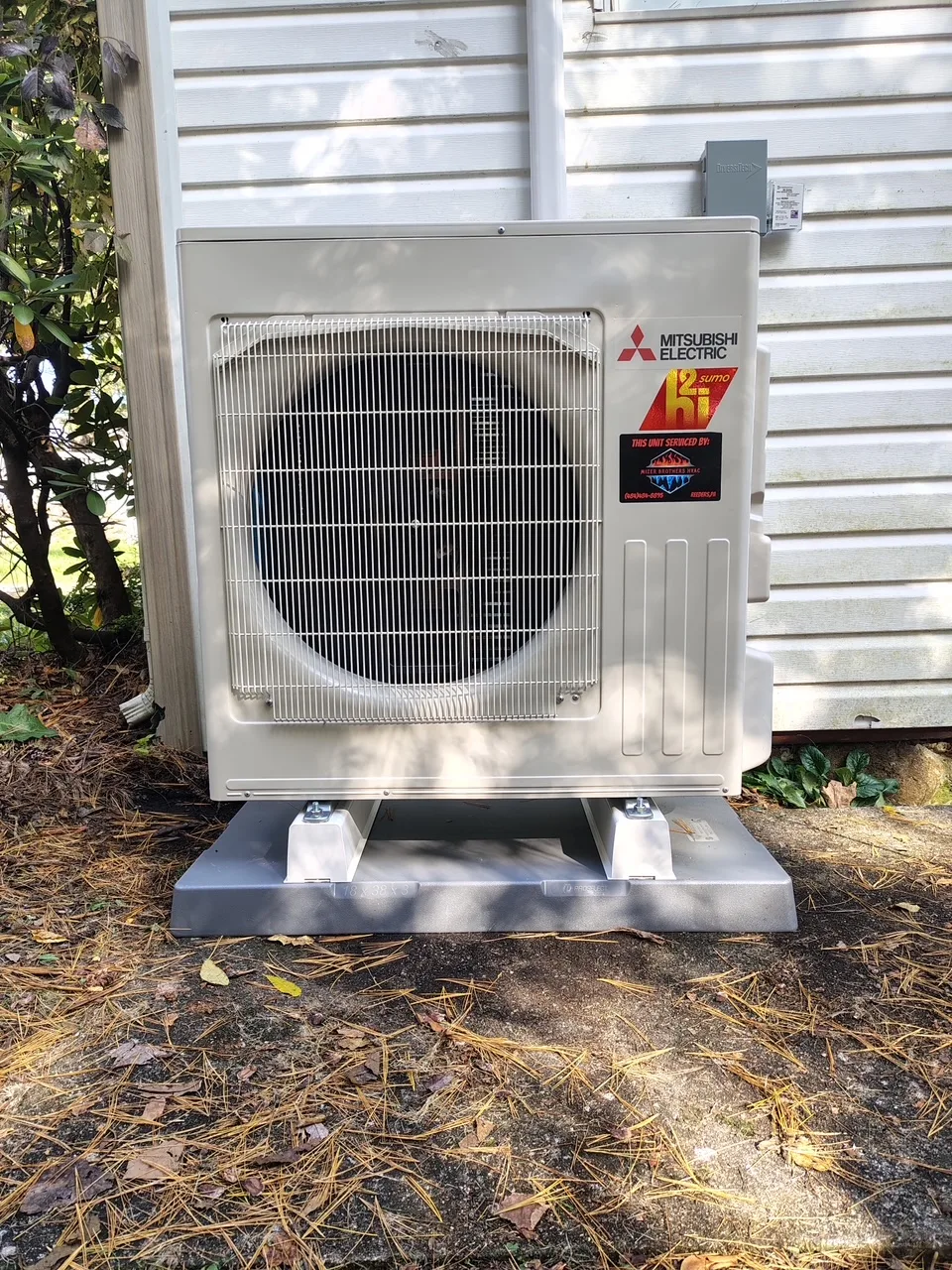 Mitsubishi Electric heat pump condenser installed on a raised pad beside a customer's home