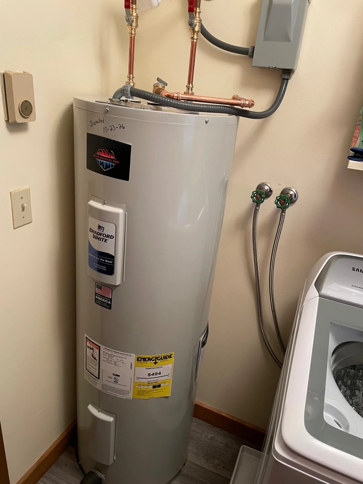 Bradford White electric water heater installed in a laundry room beside a washing machine