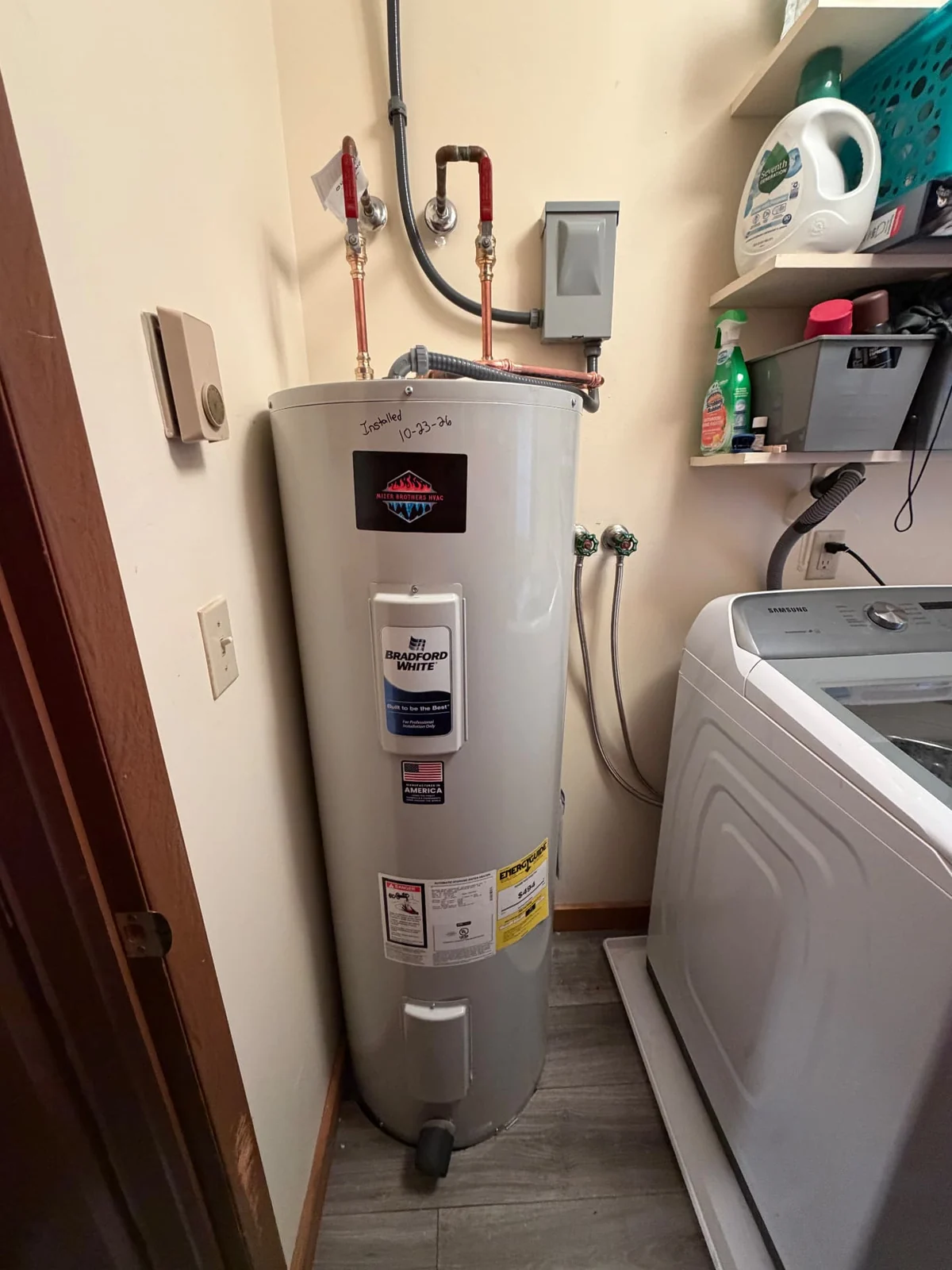 Bradford White electric water heater installed in a utility nook, shown full length from the supply pipes to the drain valve